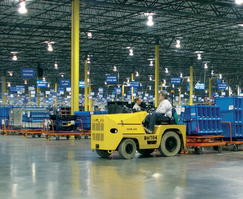Yellow Harlan tractor hauling blue containers within a warehouse.