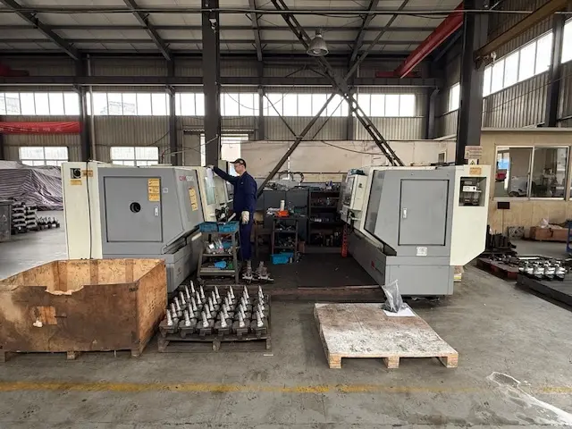 Factory technician operating a CNC lathe in a precision machining facility with rows of finished metal components on pallets.