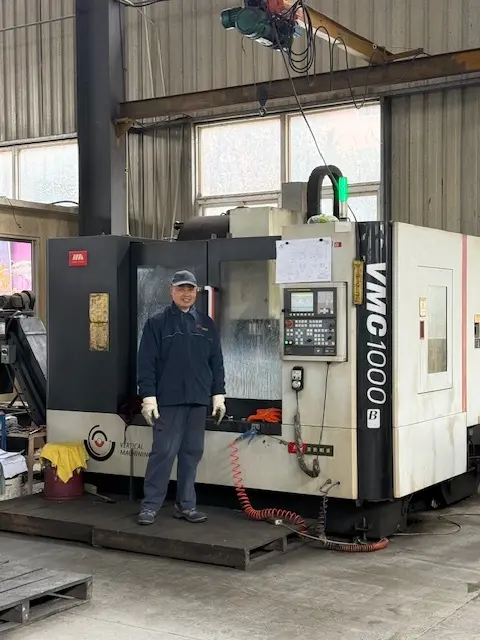 Experienced technician standing with a VMC 1000 vertical machining center in a precision CNC engineering workshop.