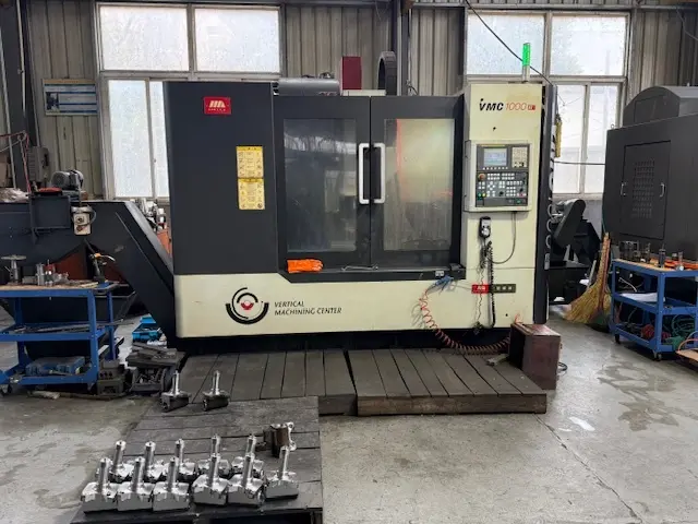 High-precision VMC 1000 vertical machining center in a CNC fabrication shop with finished metal hardware components ready for inspection.