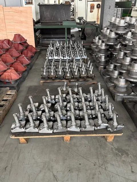 Large-scale inventory of precision-machined steel spindles and cast iron housings organized on pallets in a metal manufacturing facility.