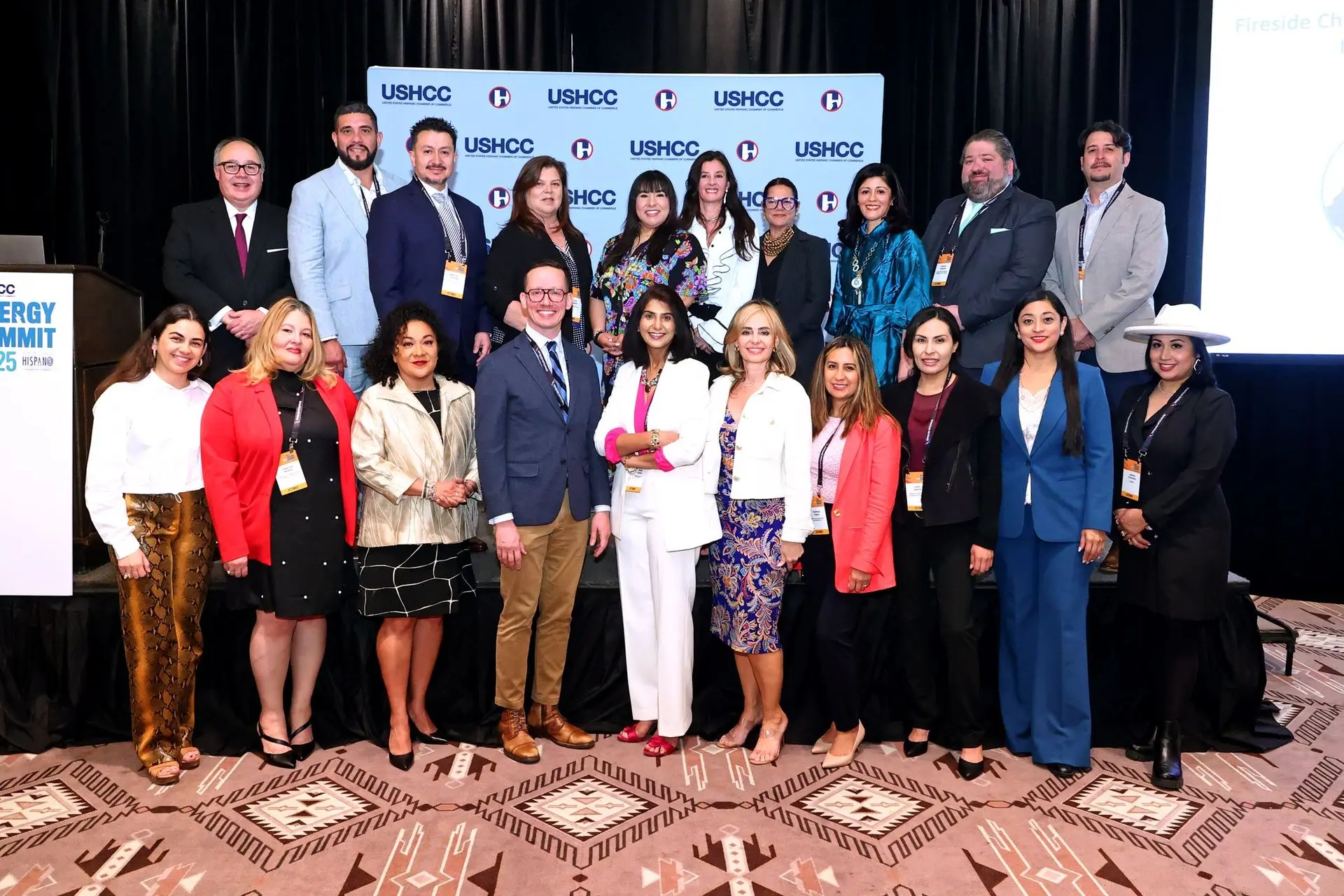 A large group of professional men and women pose together for a commemorative photo on a stage at the USHCC Energy Summit.