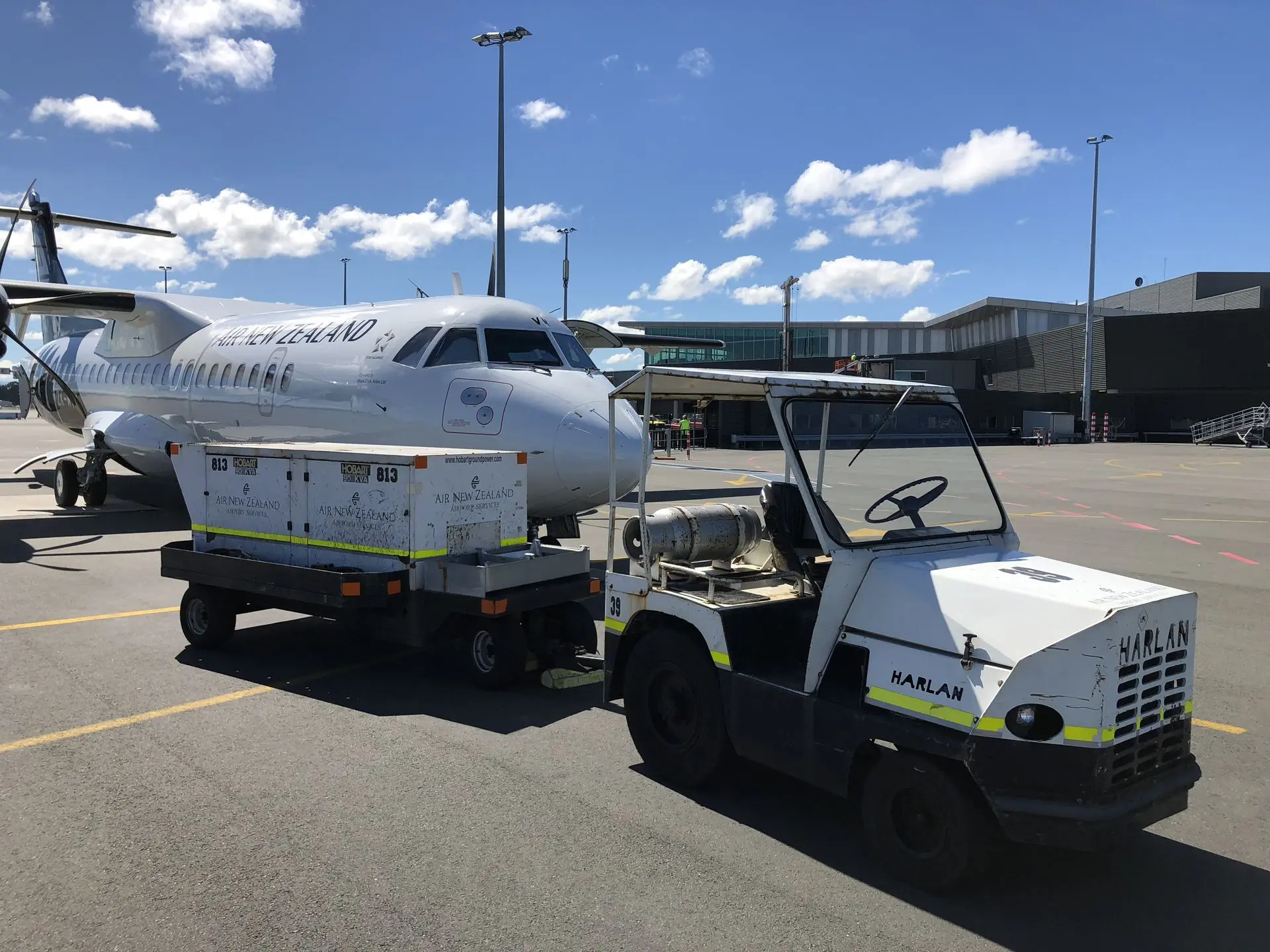 A Harlan aircraft tug towing a ground power unit for an Air New Zealand flight, demonstrating the global impact of specialized tractor machinery in international aviation services.