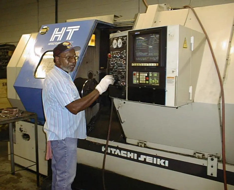 A skilled technician operating a Hitachi Seiki CNC lathe in a manufacturing workshop, demonstrating the precision engineering and high-quality production standards used to build durable industrial tractors.