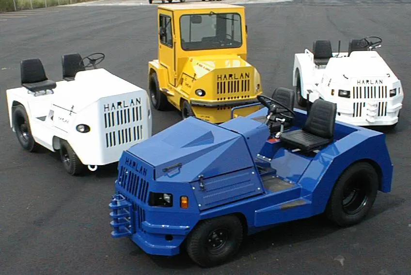 A diverse lineup of Harlan aircraft tugs in various colors and configurations, demonstrating the long-term evolution of heavy-duty airport towing equipment and multi-purpose industrial tractors.