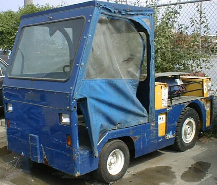 A blue Harlan HLE electric tractor with a weather-protected enclosed cab, demonstrating robust engineering for year-round airport ground handling and cargo logistics.