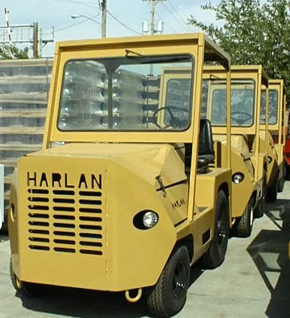 A fleet of yellow Harlan HTA50 tow tractors featuring protective overhead guards and windshields, highlighting the durable build and safety-first design of industrial airport tugs.